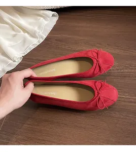 Détail de ballerines en daim rouge avec bout rond et décoration de nœud délicate