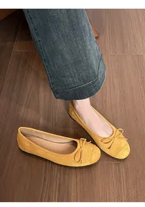 Close-up van gele suède ballerina's met strikje op bruine houten vloer