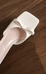 Primer plano de sandalias blancas con punta cuadrada, lazo elegante y cuero microfibra