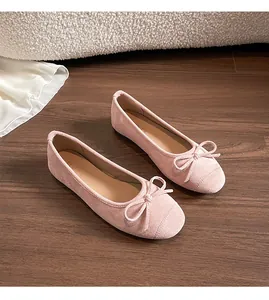 Detailopname van roze suède ballerina's met strikdetail op een houten vloer