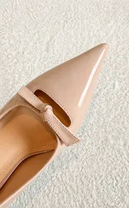 Détail macro de la finition en cuir verni brillant et du nœud sur l'escarpin beige pointu