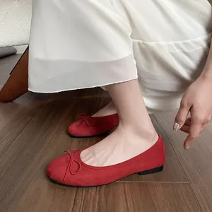 Ballerines rouges en daim à bout rond et nœud décoratif sur un parquet élégant