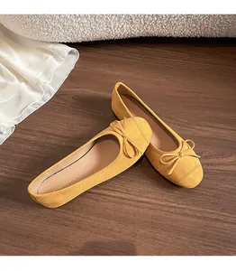 Detailopname van gembergele suède ballerina's met strikje op een donkere houten vloer