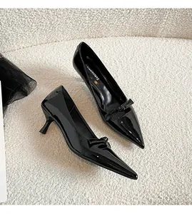 Gros plan d'escarpins noirs en cuir verni avec nœud posés sur un tissu de laine blanche