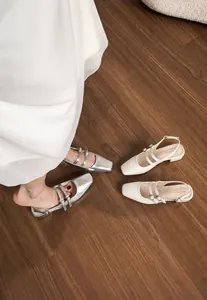 Détail de sandales slingback argent et beige sur sol en bois avec robe blanche