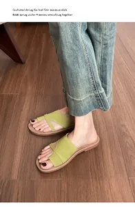Flat grass green suede slide sandals worn by a model on a brown wooden floor background