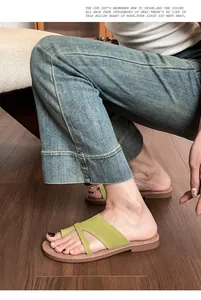 Close-up of green leather flat toe-ring sandals paired with blue wide-leg jeans