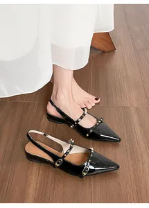 Detalle de los zapatos destalonados en charol negro con tiras de tachuelas doradas