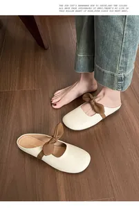 Κοντινό πλάνο από κρεμ μυτερά mules με καφέ φιόγκο σε σκούρο ξύλινο δάπεδο
