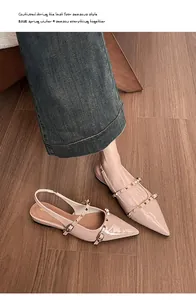 Primer plano de sandalias planas de punta rosa nude con tachuelas doradas y acabado de charol