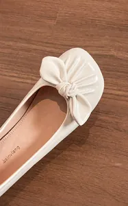 Détail de ballerines crème en microfibre avec un grand nœud décoratif sur cuir souple