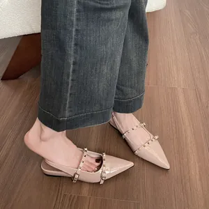 Sandalias planas beige de punta fina con remaches y correas mostradas en modelo