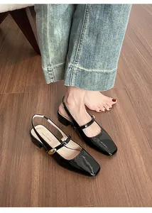Close-up of black patent leather Mary Jane shoes with square toe and gold buckle detail