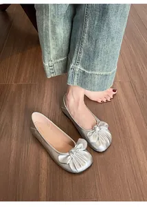 Détail de ballerines argentées avec nœud plissé sur un sol en bois sombre élégant