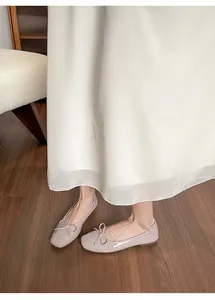 Detail von beigen Ballerinas mit eckiger Zehenpartie, Schleife und glänzender Lackoberfläche
