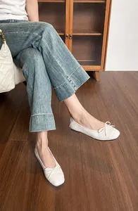Nahaufnahme eleganter weißer Ballerinas mit quadratischer Spitze und Schleife auf Holzboden