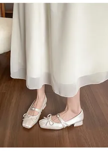 Chic cream Mary Jane shoes with bow detail and block heel shown on a wooden floor