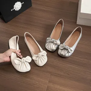 Ballerines souples en cuir avec nœud décoratif en beige et argent sur parquet en bois