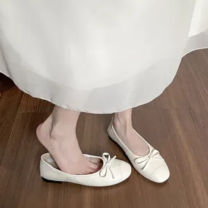 Ballerines tressées blanc cassé avec nœud portées par un mannequin sur sol en bois