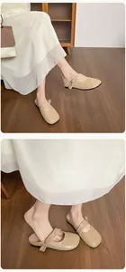 Dettaglio ravvicinato di sabot beige piatti con nodo decorativo e abito bianco
