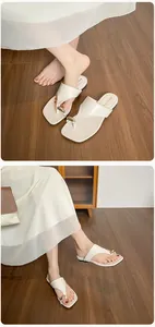 Close-up of cream square-toe flip-flops with elegant oval gold buckle detail