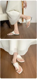 Detailed close-up of cream flip-flops featuring a stylish large gold metal buckle