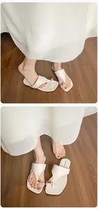 Detail view of cream-white square-toe flip flops with gold droplet buckle on feet