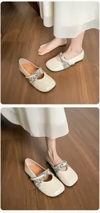 Dettaglio di ballerine beige con cinturini incrociati a fiori su pavimento in legno