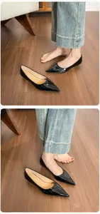Vista detallada de zapatos planos negros de punta con acabado brillante sobre suelo de madera