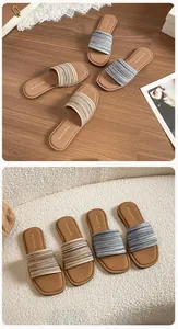 Détail de mules plates à bout carré avec bride tissée sur parquet et fond blanc doux