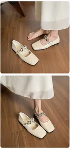 Close-up of square-toe cream Mary Jane flats with sparkling rhinestone flower buckles
