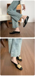 Makro-Detail der schwarzen Lackleder-Mules mit quadratischer Spitze und goldener Schnalle