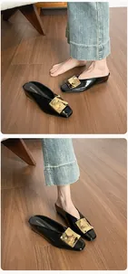 Nahaufnahme schwarzer Lackleder-Mules mit eckiger Zehenpartie und goldener Metallschnalle