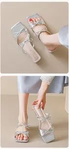 Macro detail of silver square-toe flat sandals with bow accents and metallic texture