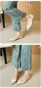 Details cremefarbener flacher Schuhe mit Schleife und Goldnieten auf strukturiertem Leder