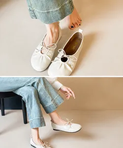 Close-up of white gathered leather ballet flats with bow detail paired with blue jeans