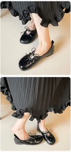Detail of glossy black ballet flats with delicate bow and elasticated edge on model