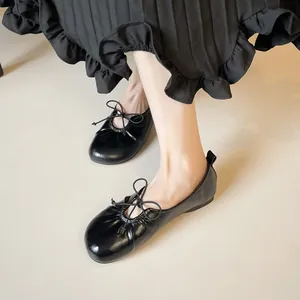 Glossy black ballet flats with round toe and bow detail worn with a pleated skirt