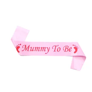 Detailed view of silky pink satin Mommy To Be sash with red lettering and baby footprints