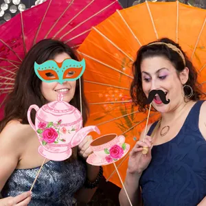 Frauen mit Foto-Requisiten zum Thema Tee-Party mit Rosendruck-Teekannen und Masken