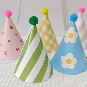 Detail of colorful party cone hats with pom-poms and various patterns on white grid fabric