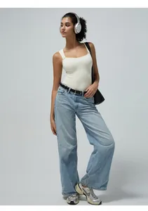 Nahaufnahme des nahtlosen beigen Rippstrick-Jumpsuits mit weit geschnittenen hellblauen Jeans