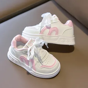Close-up of children's white sneakers featuring pink M-shaped stripes and soft soles