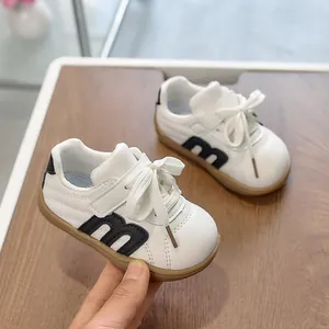 Zapatillas blancas ligeras para niños con logo m negro y suela de goma en la mano