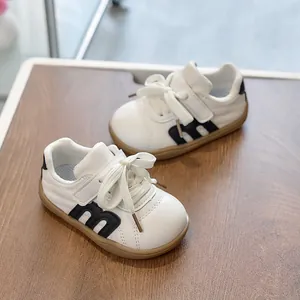 Vista superior de zapatillas blancas para niños con logo M negro sobre fondo de madera