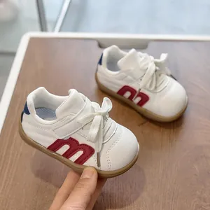 Detalle de zapatilla blanca infantil con parche M rojo y suela de goma marrón