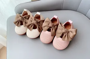 Overhead view of knit toddler shoes in beige and pink with large brown satin bows