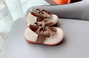 Detailed top view of cream knitted baby shoes with large brown bows and rubber soles