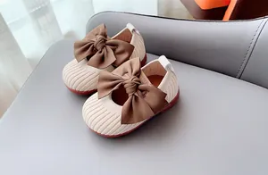 Close-up of knit toddler shoes featuring a large brown satin bow on creamy white upper