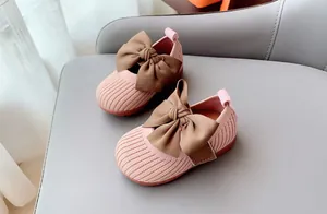 Detail of pink knitted toddler shoes featuring large brown satin bows and soft rubber soles
